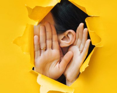 Female ear and hands close-up. Copy space. Torn paper, yellow background. The concept of eavesdropping, espionage, gossip and the yellow press.